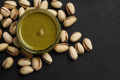 Photo of Delicious pistachio butter and nuts on black table, flat lay