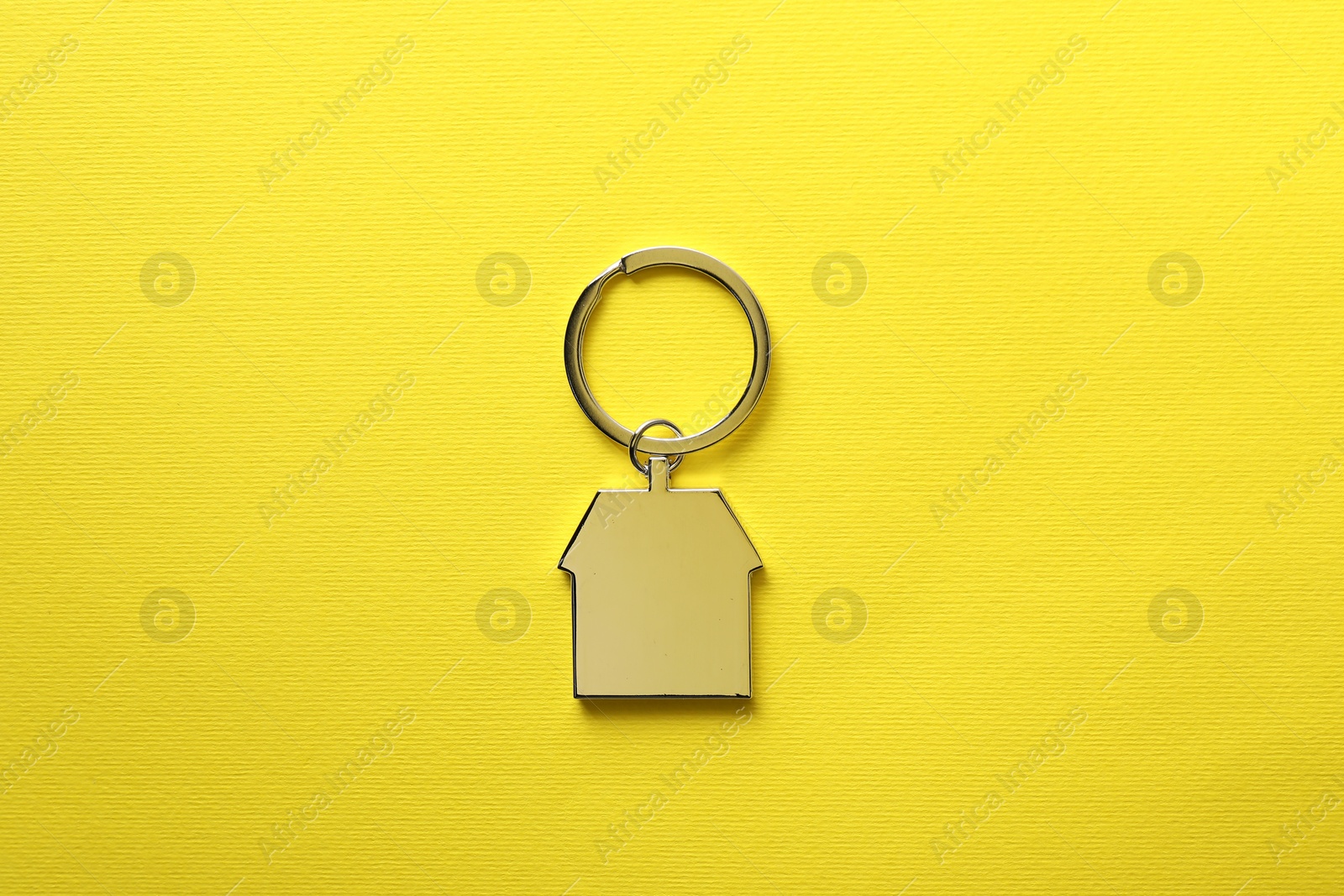 Photo of Metallic keychain in shape of house on yellow background, top view