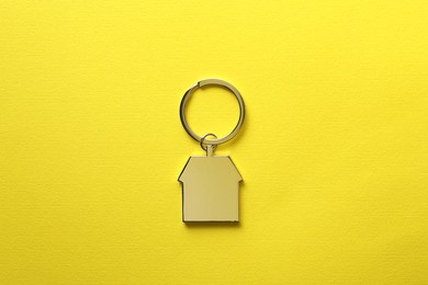 Metallic keychain in shape of house on yellow background, top view