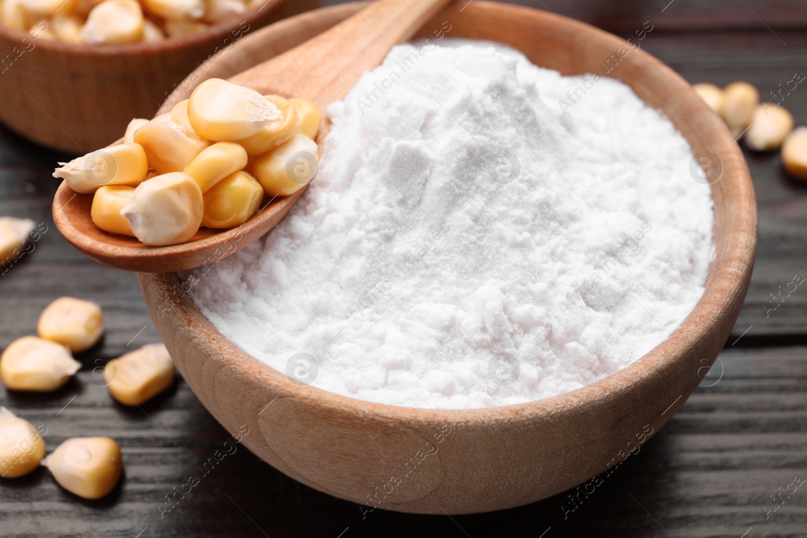 Photo of Bowl of corn starch and kernels on dark wooden table, closeup