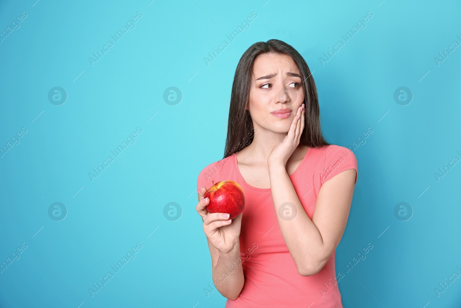 Photo of Woman with sensitive teeth holding apple on color background