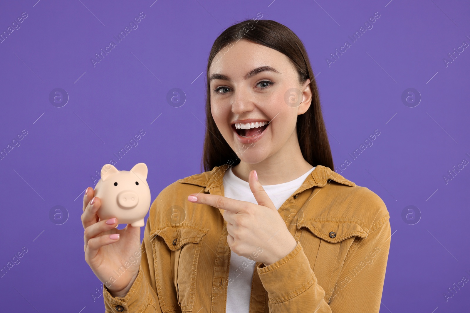 Photo of Excited woman pointing at piggy bank on purple background