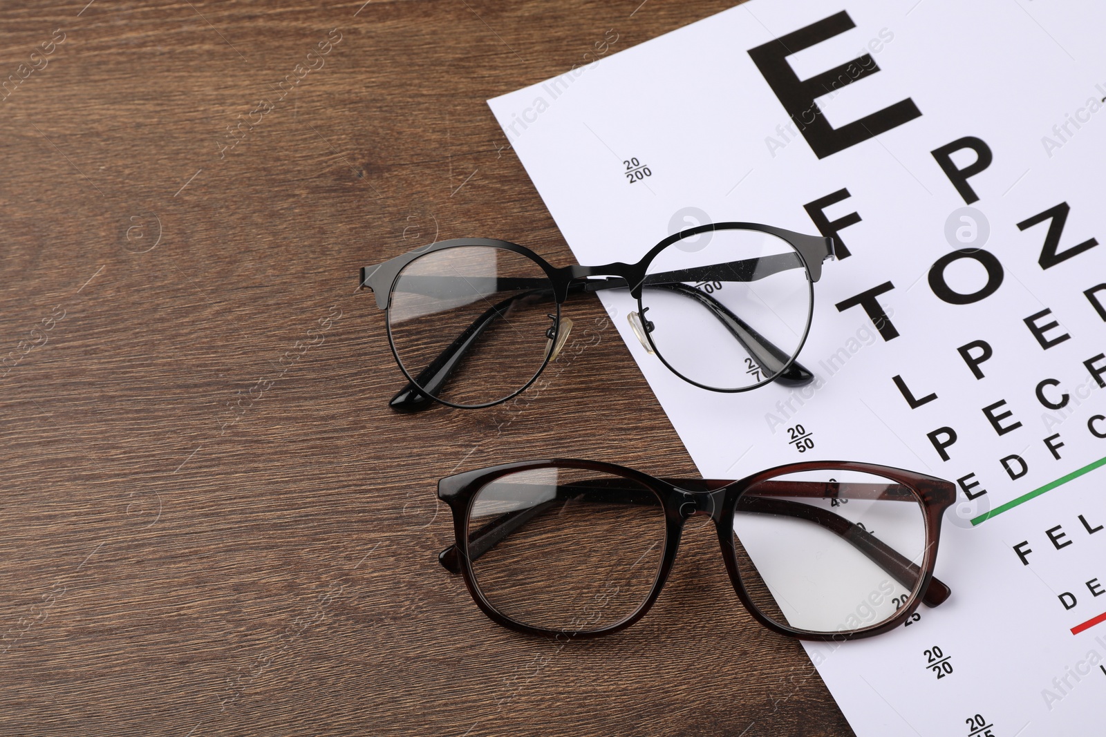 Photo of Vision test chart and glasses on wooden table, space for text