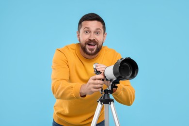 Happy astronomer with telescope on light blue background