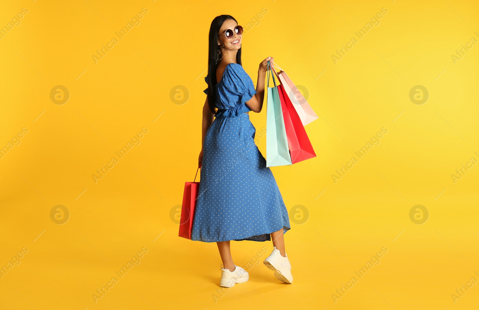 Photo of Beautiful young woman with paper shopping bags on yellow background