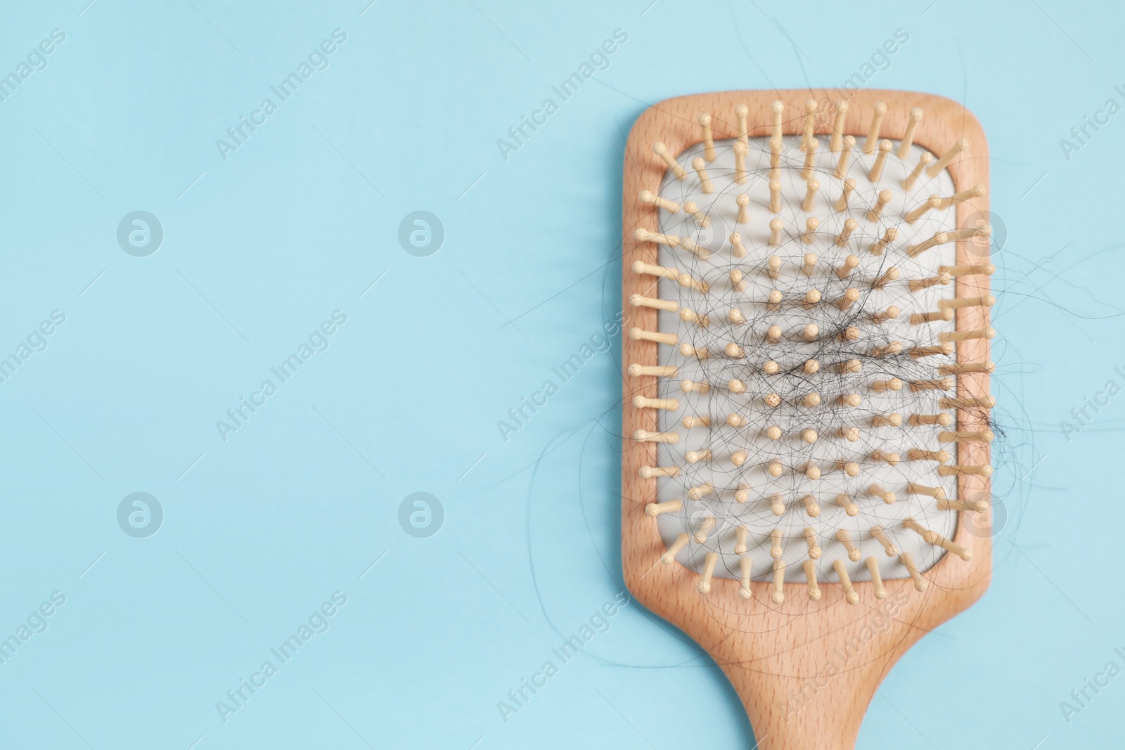 Photo of Wooden brush with lost hair on light blue background, top view. Space for text