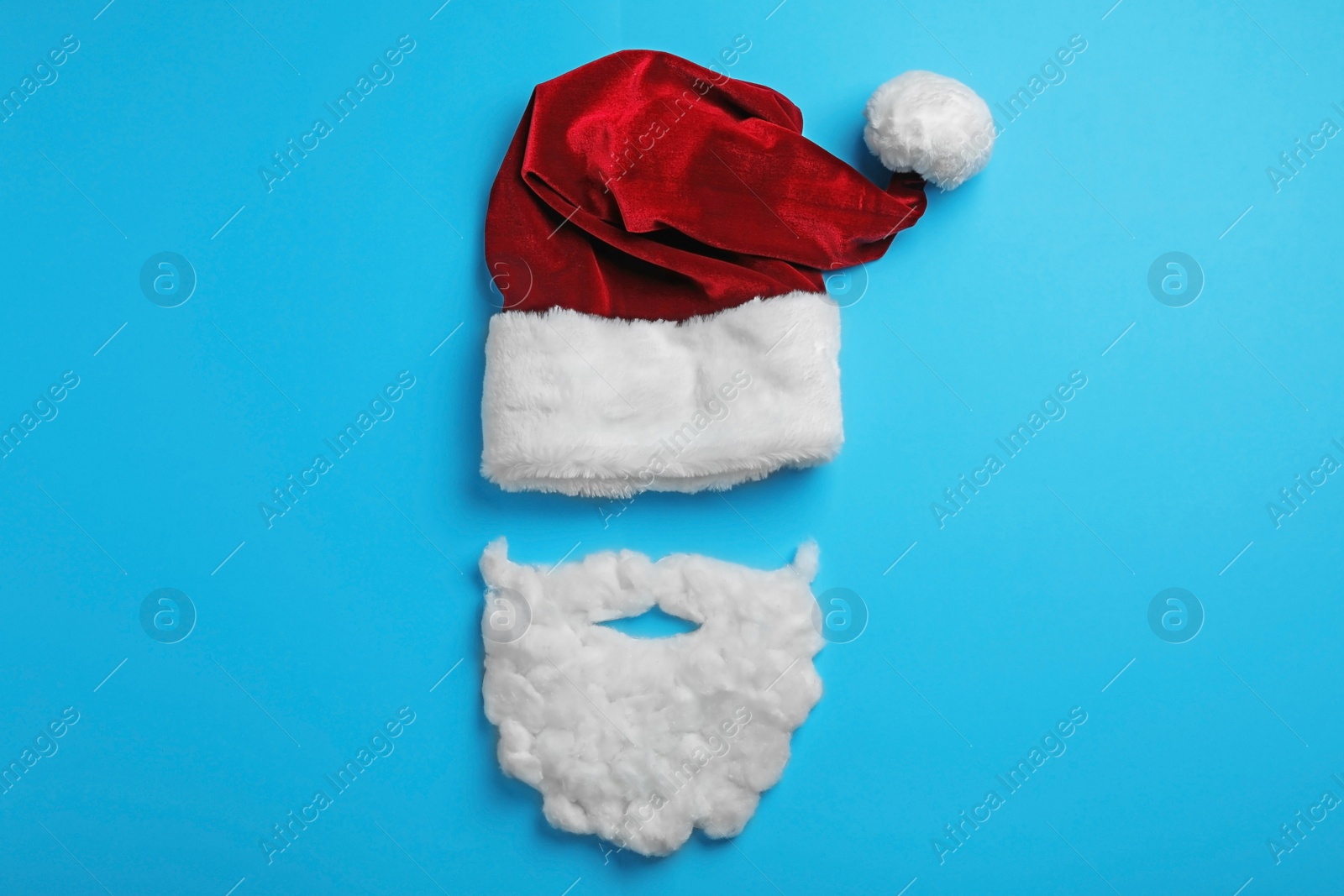 Photo of Santa Claus hat and beard on light blue background, flat lay