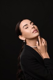 Young woman with elegant pearl jewelry on black background