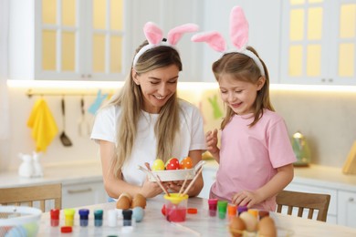 Easter celebration. Happy mother and her cute daughter with painted eggs at white marble table in kitchen