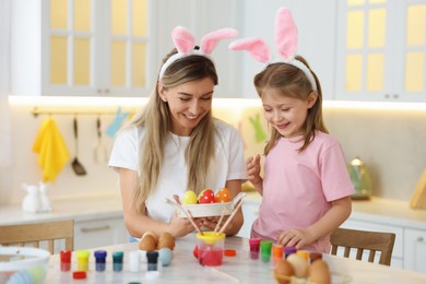 Photo of Easter celebration. Happy mother and her cute daughter with painted eggs at white marble table in kitchen