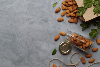 Photo of Jar with tasty almonds and green leaves on light grey table, flat lay. Space for text