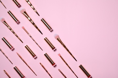 Makeup brushes and lipsticks on pink background, flat lay. Space for text