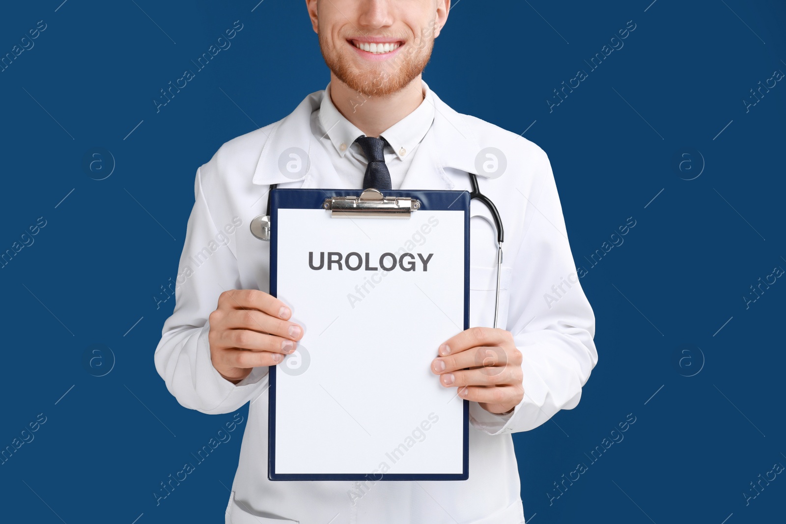 Photo of Male doctor holding clipboard with word UROLOGY on blue background, closeup