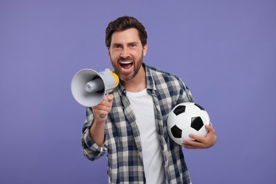 Photo of Emotional sports fan with soccer ball and megaphone on purple background