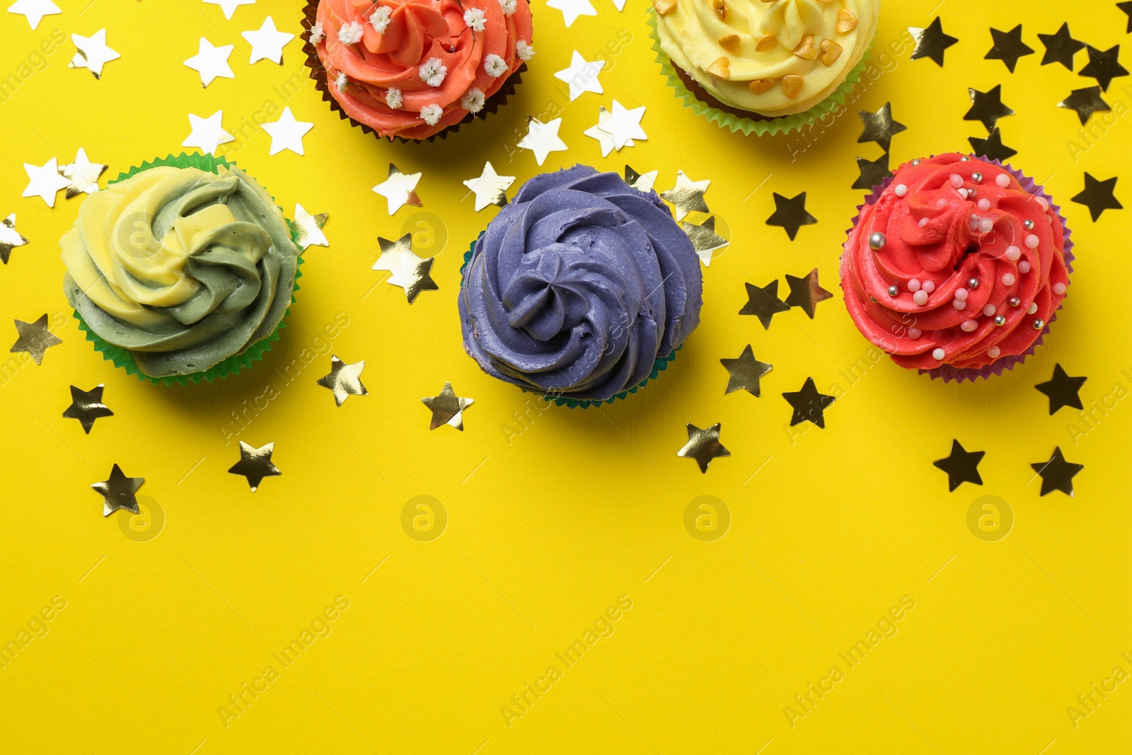 Photo of Delicious cupcake with bright cream and shiny confetti on yellow background, flat lay. Space for text