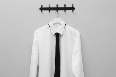 Hanger with white shirt and black tie on light grey wall