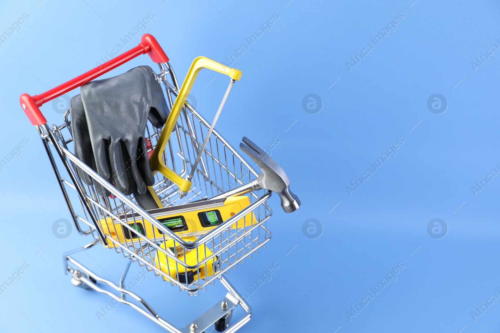 Photo of Small shopping cart with set of construction tools and gloves on light blue background. Space for text