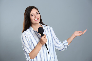 Young female journalist with microphone on grey background