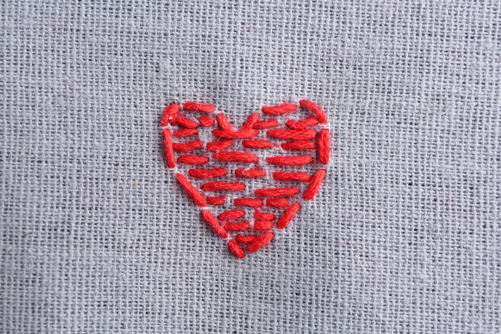 Photo of Embroidered red heart on gray cloth, top view