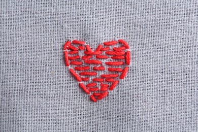 Photo of Embroidered red heart on gray cloth, top view