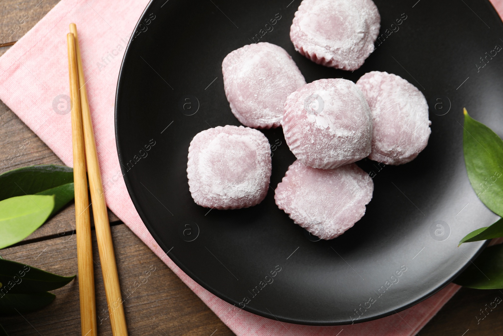 Photo of Black plate with delicious mochi and chopsticks on wooden table, flat lay. Traditional Japanese dessert