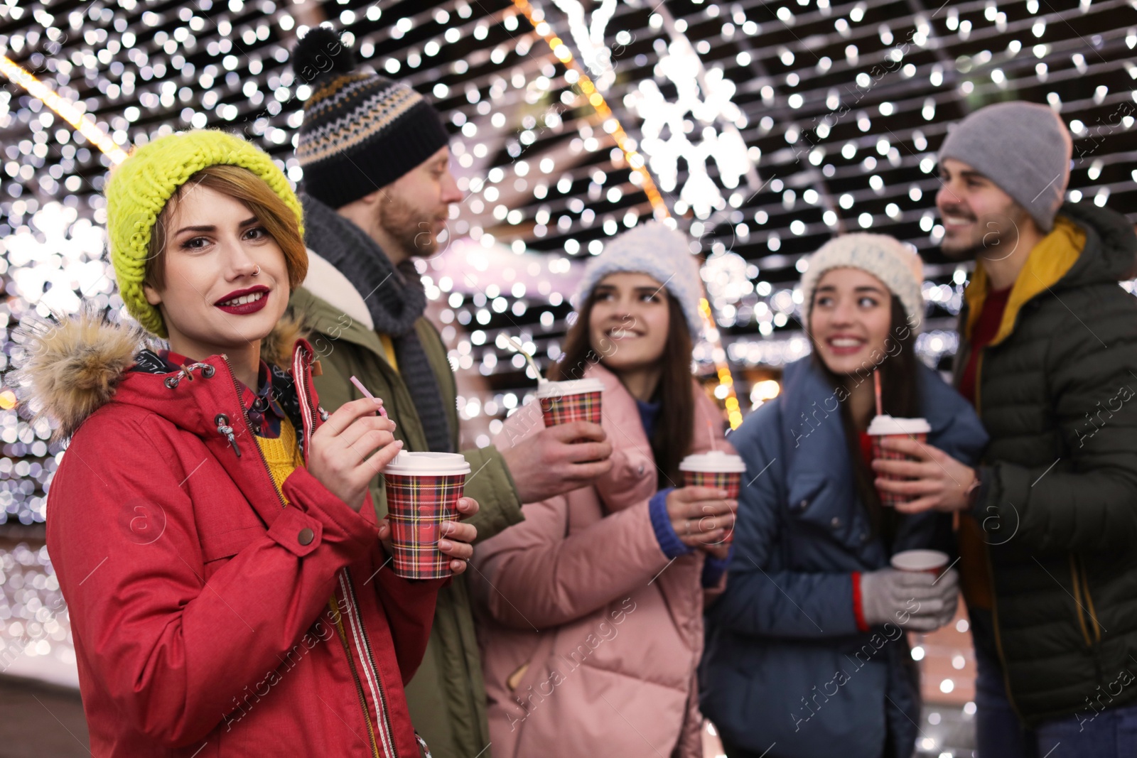 Photo of Happy friends with cups of mulled wine at winter fair