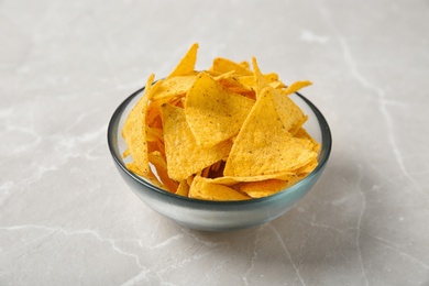 Photo of Tasty mexican nachos chips in glass bowl on grey table