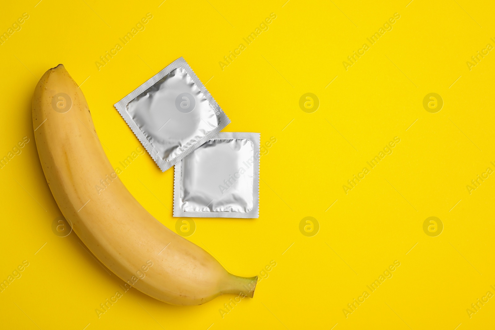 Photo of Condoms with banana and space for text on yellow background, flat lay. Safe sex