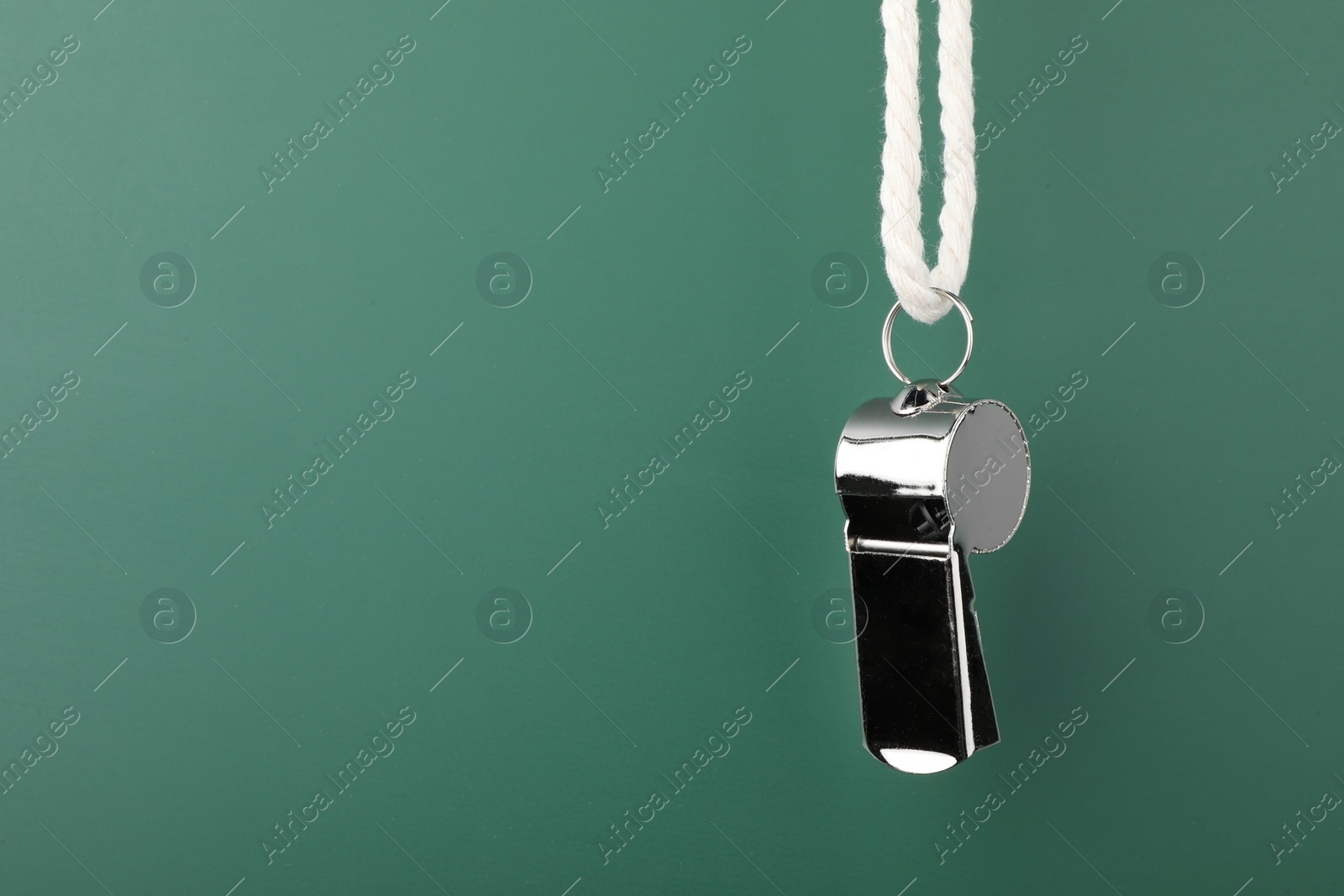 Photo of Referee equipment. Metal whistle on dark green background, closeup and space for text