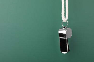 Photo of Referee equipment. Metal whistle on dark green background, closeup and space for text