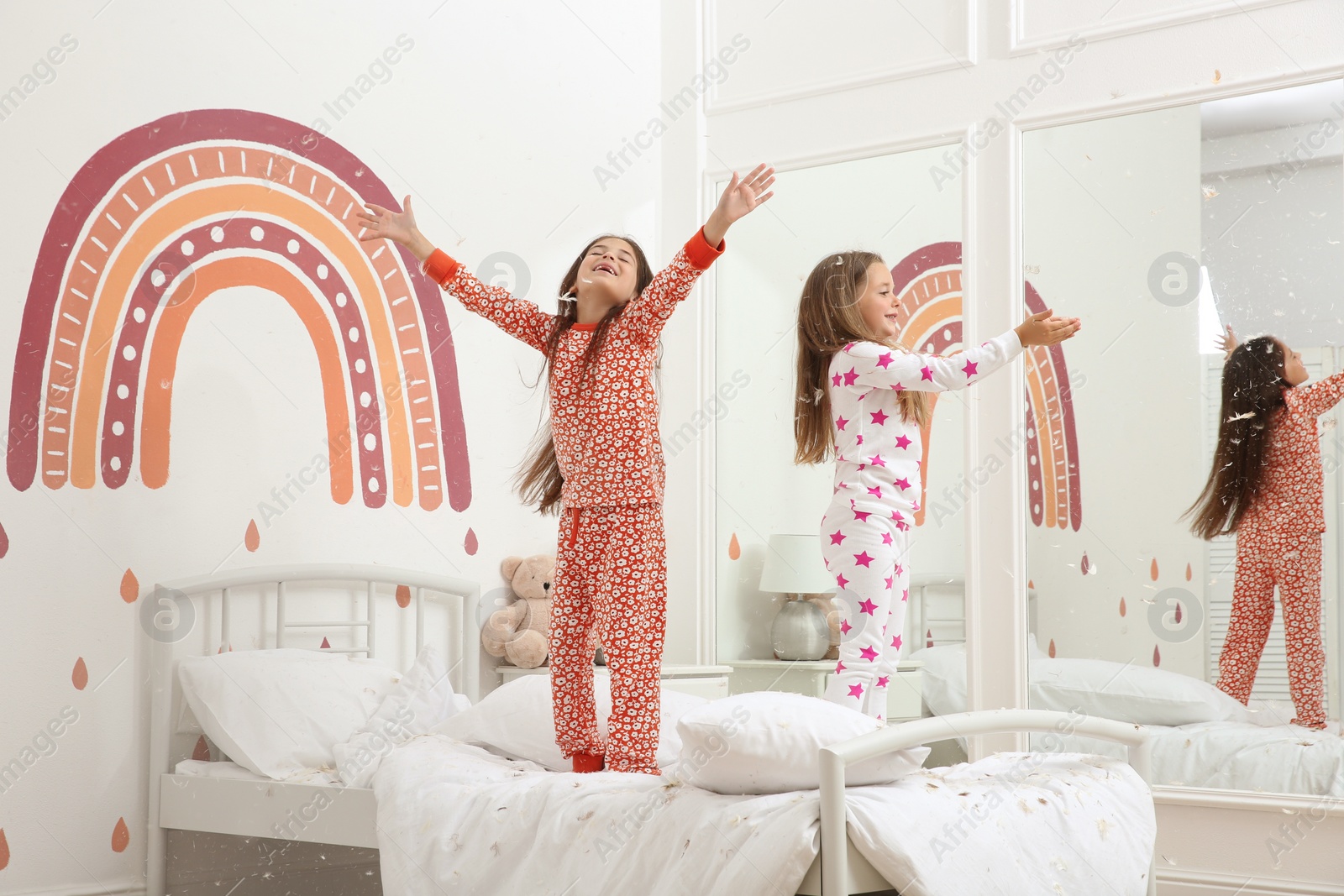 Photo of Cute little girls in pajamas playing with feathers on bed at home. Happy childhood