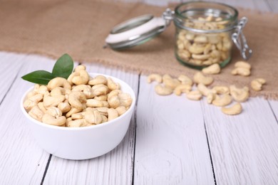 Photo of Tasty cashew nuts and green leaves on white wooden table, closeup