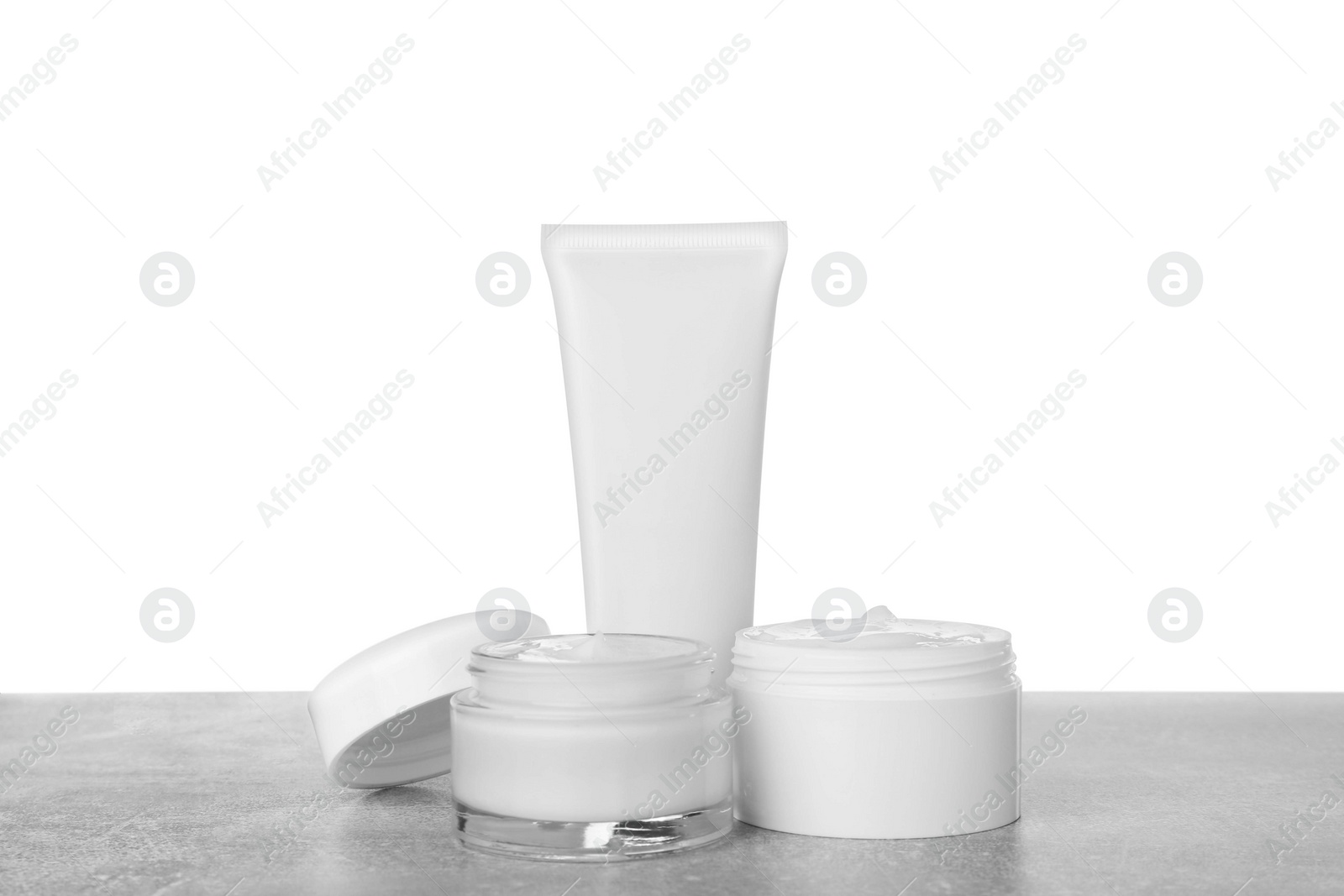 Photo of Jars and tube of hand cream on gray table against white background
