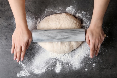 Photo of Female baker preparing bread dough at grey table, top view