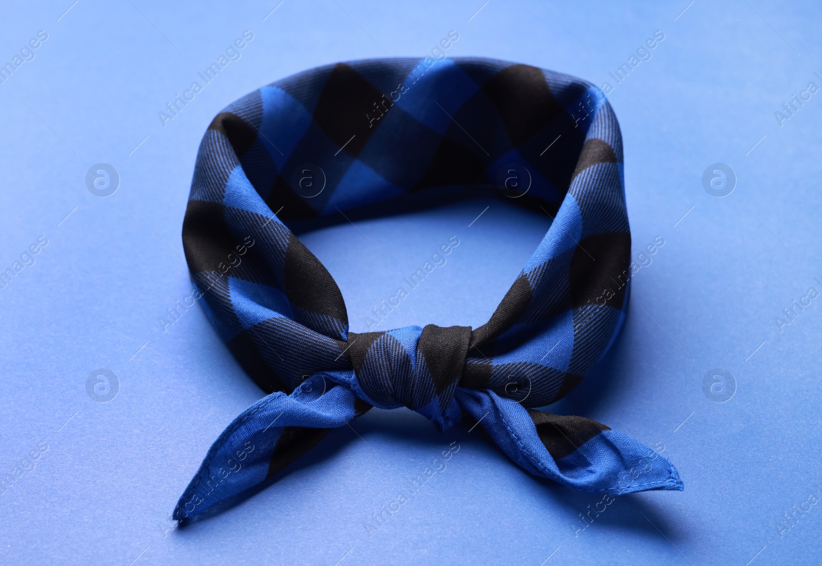 Photo of Tied bandana with check pattern on blue background, closeup