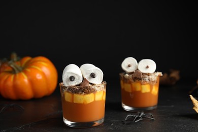 Photo of Glasses with delicious dessert decorated as monsters on black table. Halloween treat