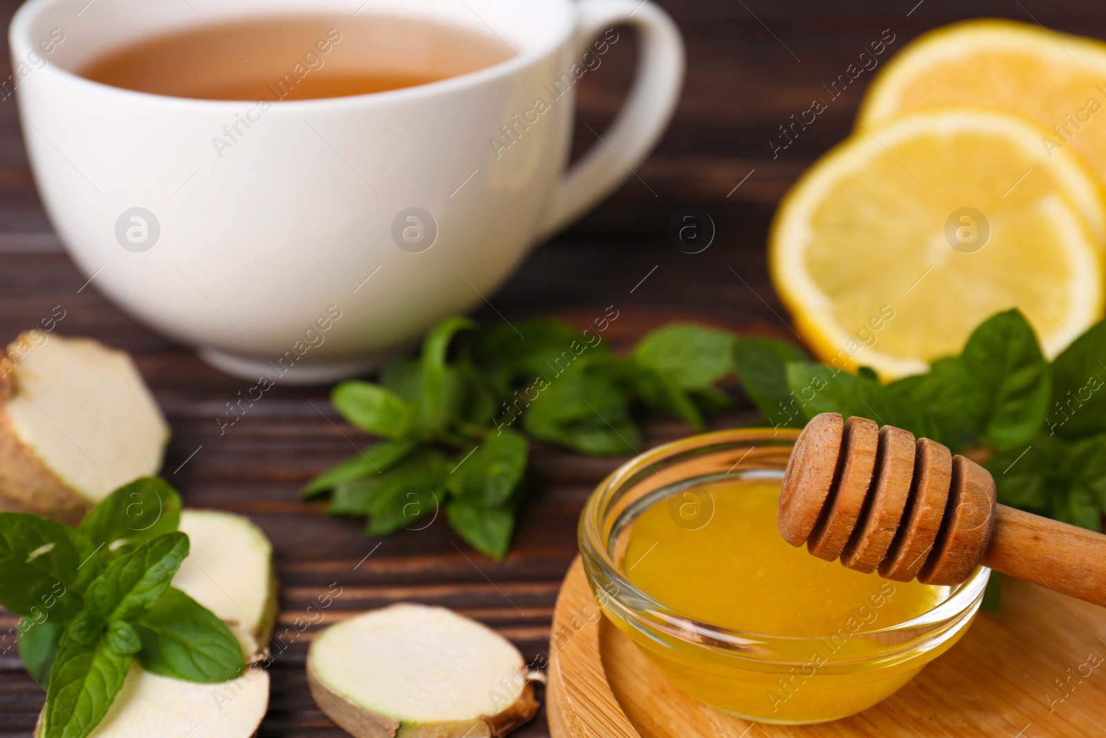 Photo of Bowl with honey for tea, lemon, mint and ginger on wooden table