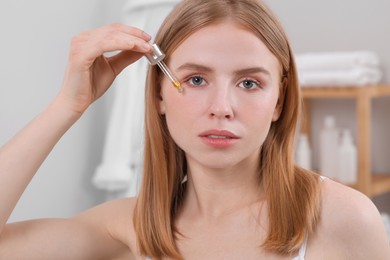 Woman applying essential oil onto face in bathroom