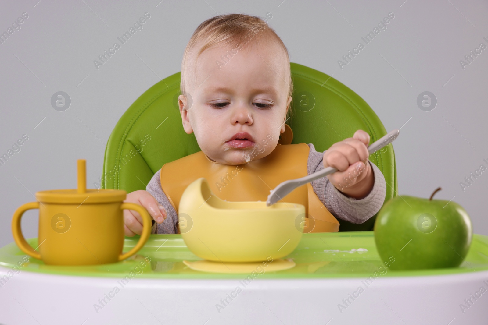 Photo of Cute little baby eating healthy food in high chair on gray background