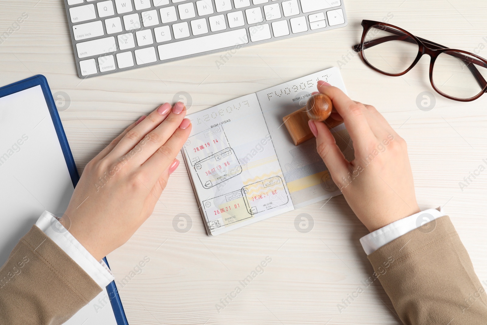 Photo of Ukraine, Lviv - September 6, 2022: Woman stamping visa page in passport at white wooden table, top view