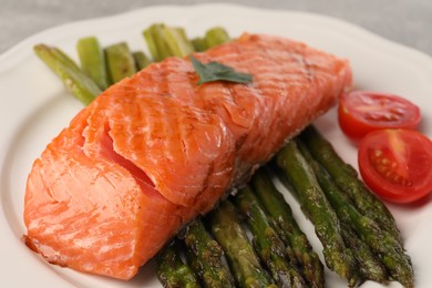 Photo of Tasty grilled salmon with tomatoes and asparagus on plate, closeup