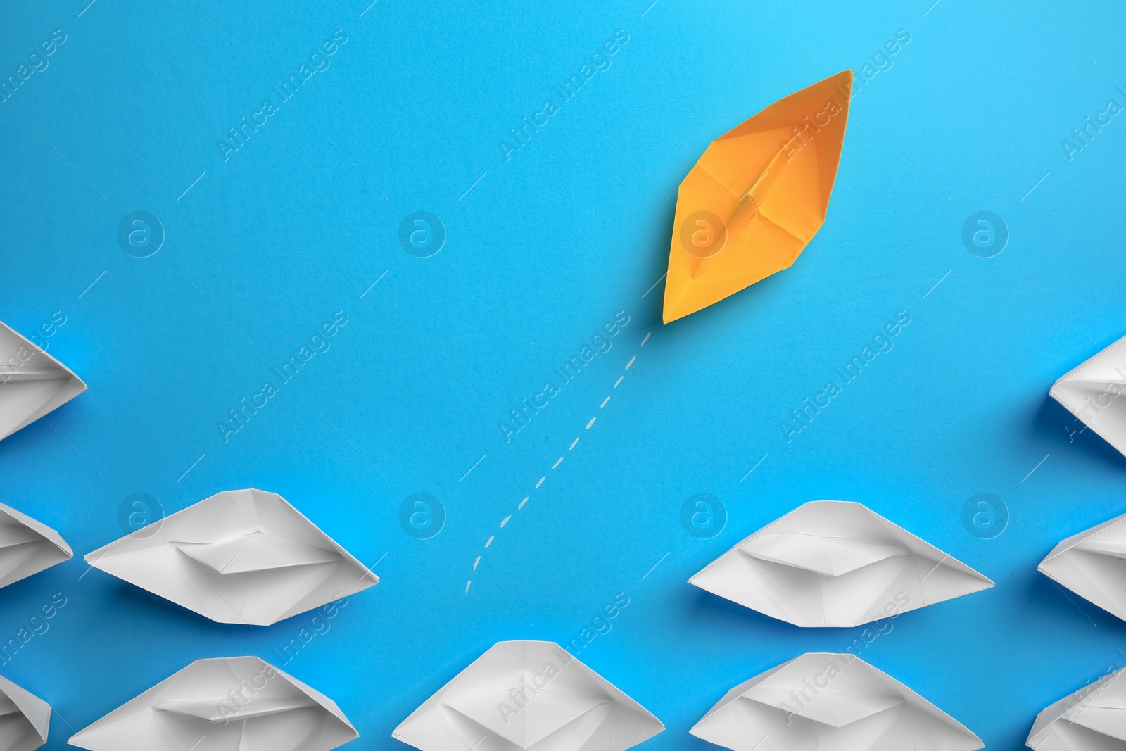 Photo of Yellow paper boat floating away from others on light blue background, flat lay. Uniqueness concept