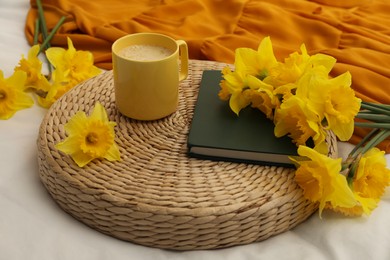 Bouquet of beautiful daffodils, book and coffee on bed