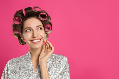 Photo of Beautiful young woman in silk bathrobe with hair curlers on pink background. Space for text