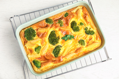 Photo of Tasty broccoli casserole in baking dish on cooling rack, top view