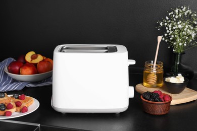 Photo of Modern toaster, bread, fresh berries and honey on black table. Tasty breakfast