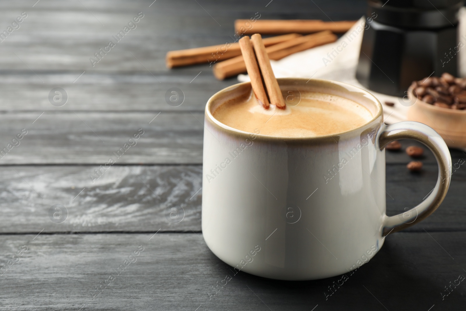 Photo of Cup of hot coffee with aromatic cinnamon on black wooden table. Space for text