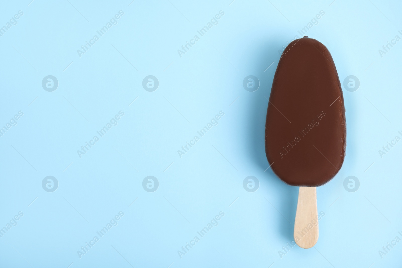 Photo of Ice cream glazed in chocolate on light blue background, top view. Space for text