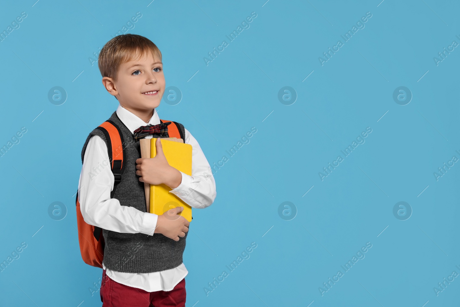 Photo of Happy schoolboy with backpack and books on light blue background, space for text