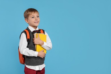 Happy schoolboy with backpack and books on light blue background, space for text